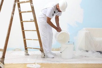 painter man at work pour into the bucket color for painting wall