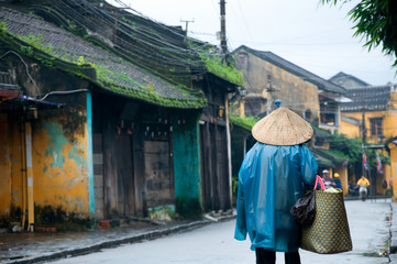 An old woman in traditional vietnamese conical hats walk on a street in Hoi An, Vietnam. Hoi An is a World Heritage Site.