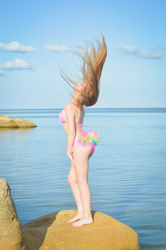 Young lady with perfect figure sunbathing standing on rock by