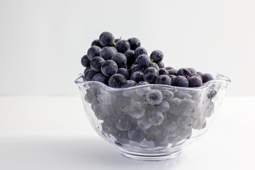 blue grapes in a glass bol on a white background