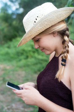 young girl writes in the telephone in the field with straw hat