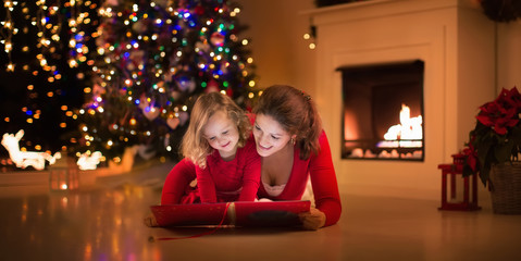 Fototapeta na wymiar Mother and daughter reading at fire place on Christmas eve