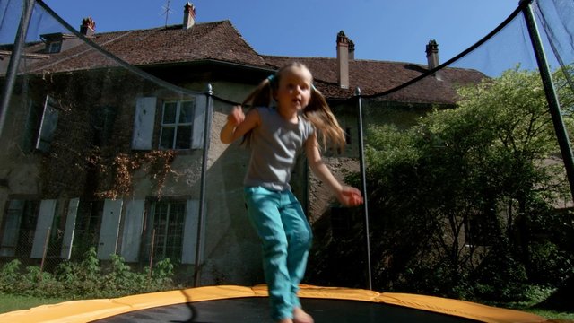 Cute little girl jumping on trampoline in the backyard