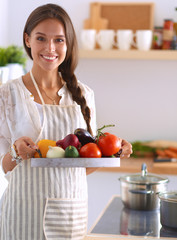 Smiling young woman holding vegetables standing in kitchen