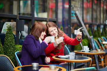 Two cheerful girls taking selfie in a Parisian cafe