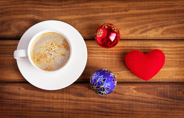 Cup of coffee, heart and christmas bubbles on wooden background.