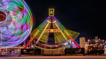 Giant Ferris Wheel and swing boat amusement ride side by side in night time shot with long exposure.