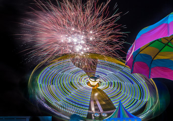Firework and amusement ride under one umbrella. Long exposure to show fireworks and motion for the ride.