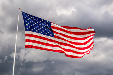 Brightly lit USA flag on a windy day against clouds