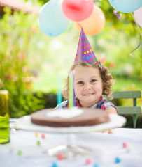 funny little girl at a garden party for her birthday, cake, colorful hat, balloon and confetti 