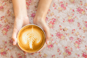 Vintage woman hands holding latte art coffee mug on flower vinta