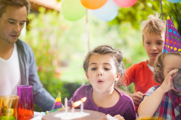 garden party with family for little girl's birthday, girl blowing the candles , the garden is decorated with balloons and colors are bright