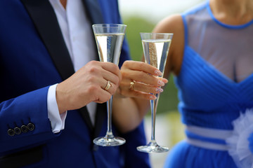 Жених в синем костюме и невеста в синем платье, стоя с бокалами в который наливают шампанское