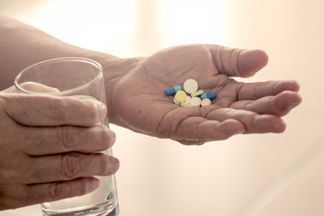 Old woman hand holding heap of pills and water glass in vintage
