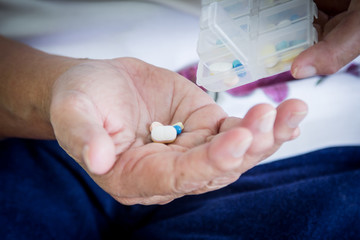 old woman hand pouring pills from a pill reminder box into her h