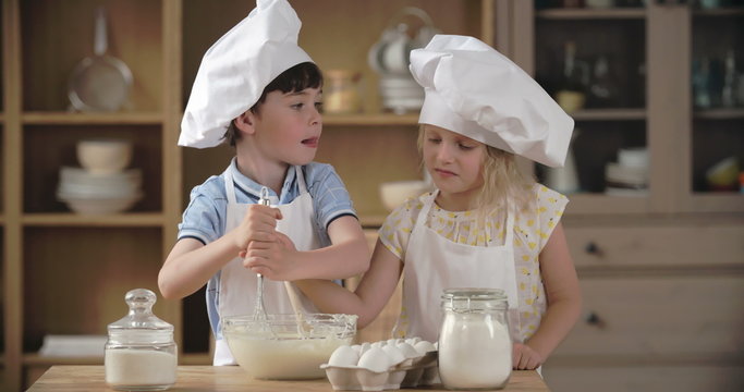 Lovely little boy and girl making dough in domestic kitchen 