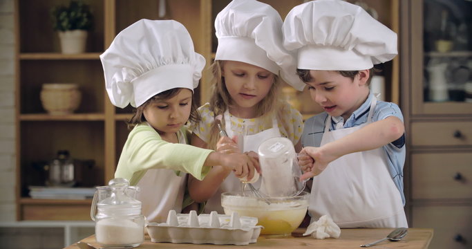 Group of lovely children pouring flour into egg mixture 