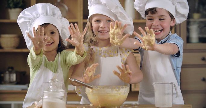 Cheerful little cooks showing hands covered with batter 