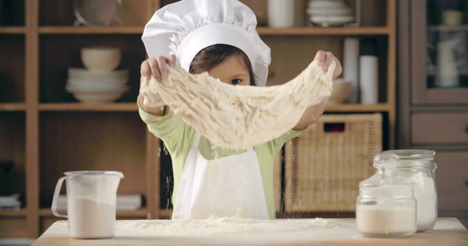 Adorable little girl in apron and chef hat kneading dough