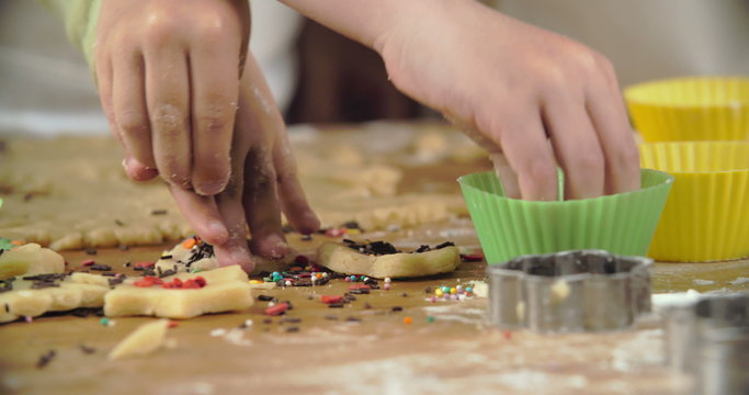 Hands of kids decorating raw cookies with multi-colored sprinkles 