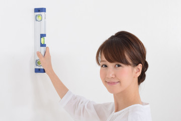 水準器で壁の歪み確認する女性
