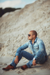 Obraz premium Guy sitting on the sand, a tanned jeans clothes