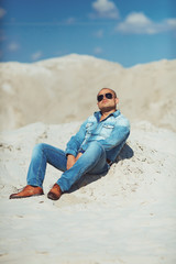 Guy sitting on the sand, a tanned jeans clothes