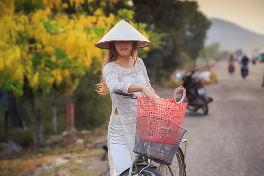blonde girl in Vietnamese dress and hat near bike on street