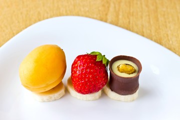 Fresh fruits and berries mix: strawberry, apricot, banana and candy on white dish