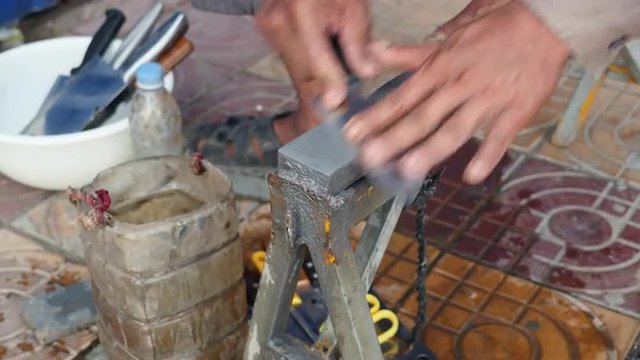 Close-up on a knife sharpener whetting a knife on the sidewalk