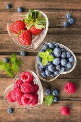 Mix of fresh berries in a glass ramekins in shape of heart, on w