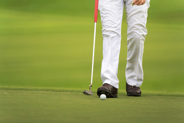 golfers walking on green with putter.