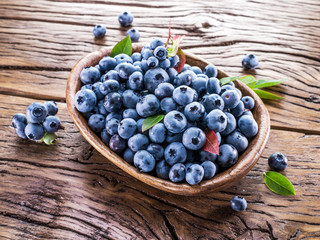 Ripe blueberries in the bowl on the wooden table.