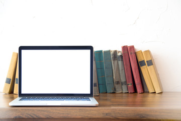 Stack of old books and laptop over wooden table, retro filtered image