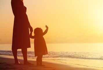 Fototapeta na wymiar mother and little daughter walking on beach at sunset