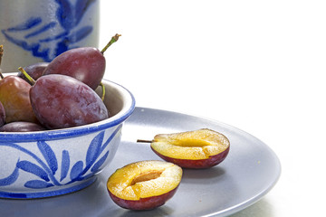 plums in blue crockery, one of them is cut, white background