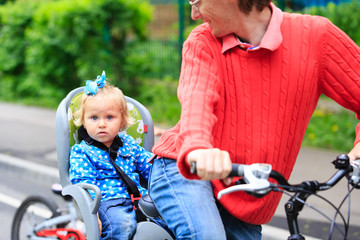 Obraz premium little girl on bike seat cycling with father in the city