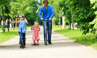 father with kids riding scooters in summer