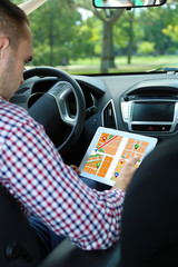 Man sitting in the car and holding tablet with map gps navigation application
