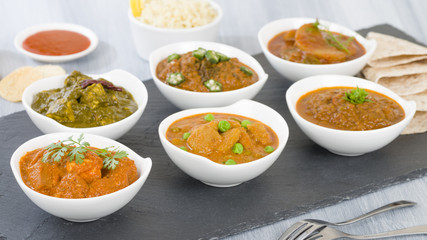 Vegetarian Curries - Selection of South Asian vegetarian curries in white bowls. Paneer Makhani, Palak Paneer, Aloo Matar, Baigan Bharta, Chilli Potatoes and Bhindi Masala, Pilau Rice and Chapattis.
