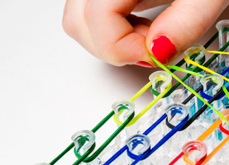 Little girl with colorful nails making a rubber loom bracelet with a hook . Hands close up. Young fashion concept