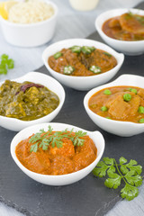 Vegetarian Curries - Selection of South Asian vegetarian curries in white bowls. Paneer Makhani, Palak Paneer, Aloo Matar, Baigan Bharta, Chilli Potatoes and Bhindi Masala, Pilau Rice and Chapattis.
