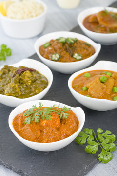 Vegetarian Curries - Selection of South Asian vegetarian curries in white bowls. Paneer Makhani, Palak Paneer, Aloo Matar, Baigan Bharta, Chilli Potatoes and Bhindi Masala, Pilau Rice and Chapattis.
