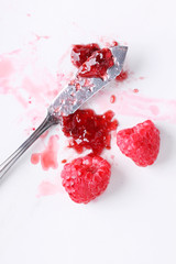 Raspberry jam and raspberry on marble table.