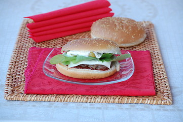 panino hamburger con carne, insalata, formaggio, ketchup su tovaglietta di paglia e tovaglioli rossi. foto in orizzontale.