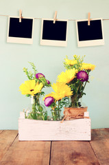 blank empty instant photos hang on a rope over summer bouquet of flowers