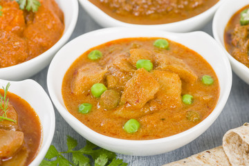 Aloo Matar - Potatoes and green peas cooked in a mild creamy tomato gravy. Chapattis and other vegetarian curries on background.
