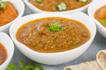 Baigan Bharta - Roasted mashed aubergines cooked with onions, tomatoes and spices. Chapattis and other vegetarian curries on background.
