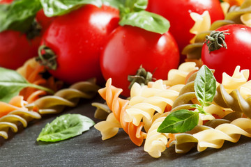 Dry colored fusilli pasta, tomatoes and basil, selective focus
