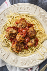 spaghetti with delicious meatballs made from ground beef in a spicy tomato sauce in a plate with inscription pasta on wooden rustic background, top view